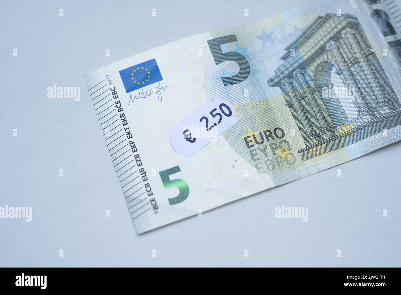 Fünf-Euro-Banknote mit 2 Euro 5 Cent Preisschild. Selektiver Fokus auf Etikett. Inflation in Europa, Hyperinflation, Abwertung des fiat-Geldkonzepts. Stockfoto