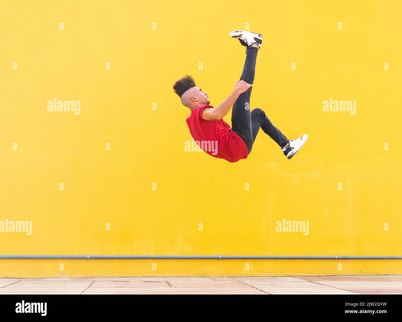 Männchen springen an der gelben Wand und zeigen einen Salto, während sie an sonnigen Tagen in der Stadt parkour Stockfoto