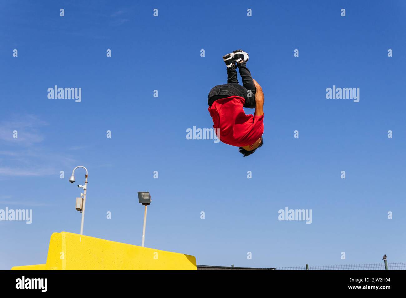 Der Mann springt vom Gebäuderand und zeigt einen Salto, während er an sonnigen Tagen in der Stadt parkour Stockfoto