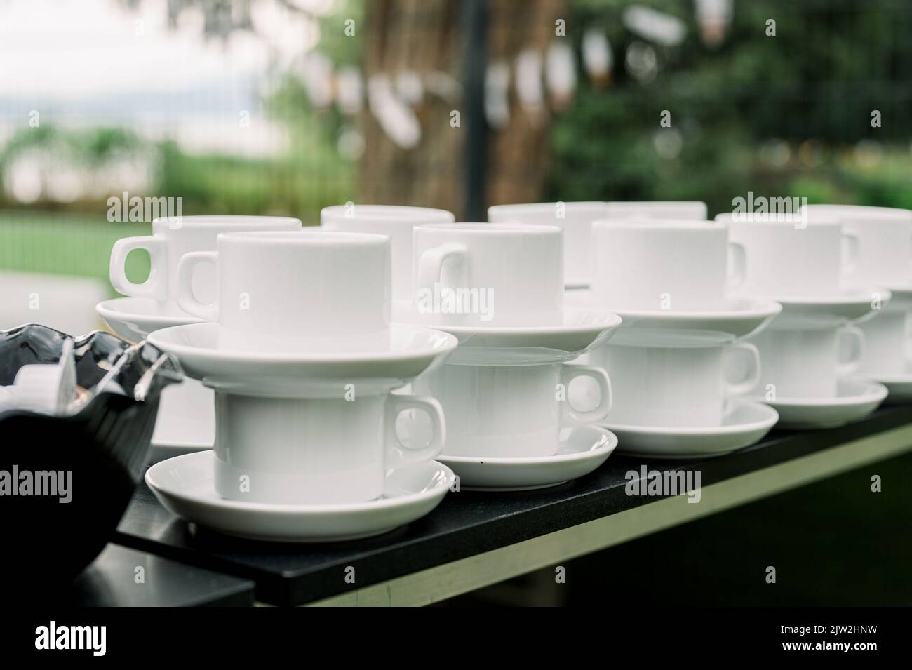 Stapel weißer Keramikbecher mit Untertassen, die auf der Theke neben der Schüssel mit Mini-Kaffeesahne im Café im Freien angeordnet sind Stockfoto
