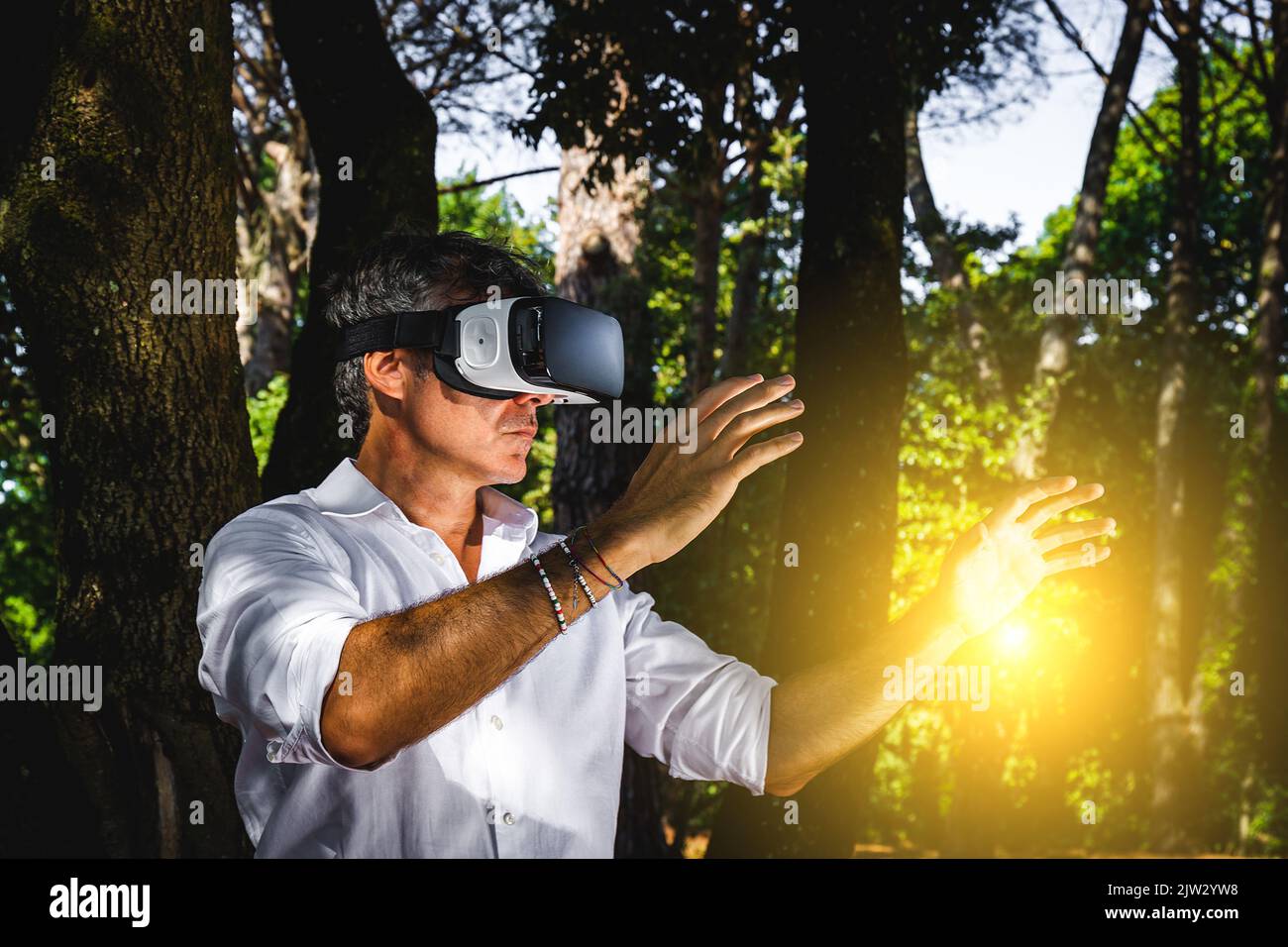 Der junge Mann nutzt einen Virtual-Reality-Betrachter im Park. Der gutaussehende Geschäftsmann arbeitet mit einem Virtual-Reality-Betrachter im Freien. Stockfoto