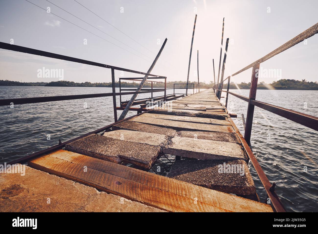 Alte beschädigte Brücke über Wasser des Sees an sonnigen Tag. Stockfoto
