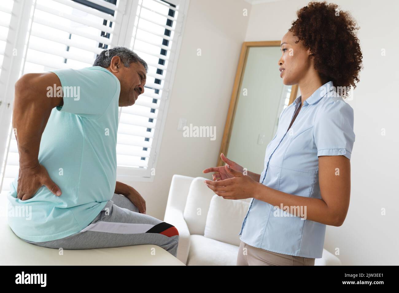 Physiotherapeutin mit gemischter Rasse im Gespräch mit einem älteren Mann, der seinen Rücken hielt Stockfoto