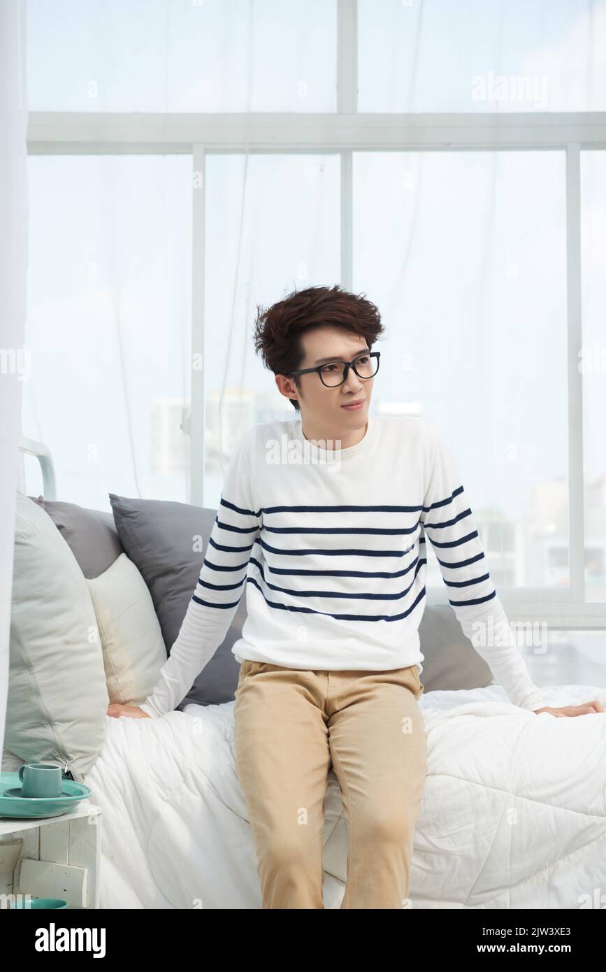 Hübscher junger asiatischer Mann, der auf seinem Bett sitzt Stockfoto