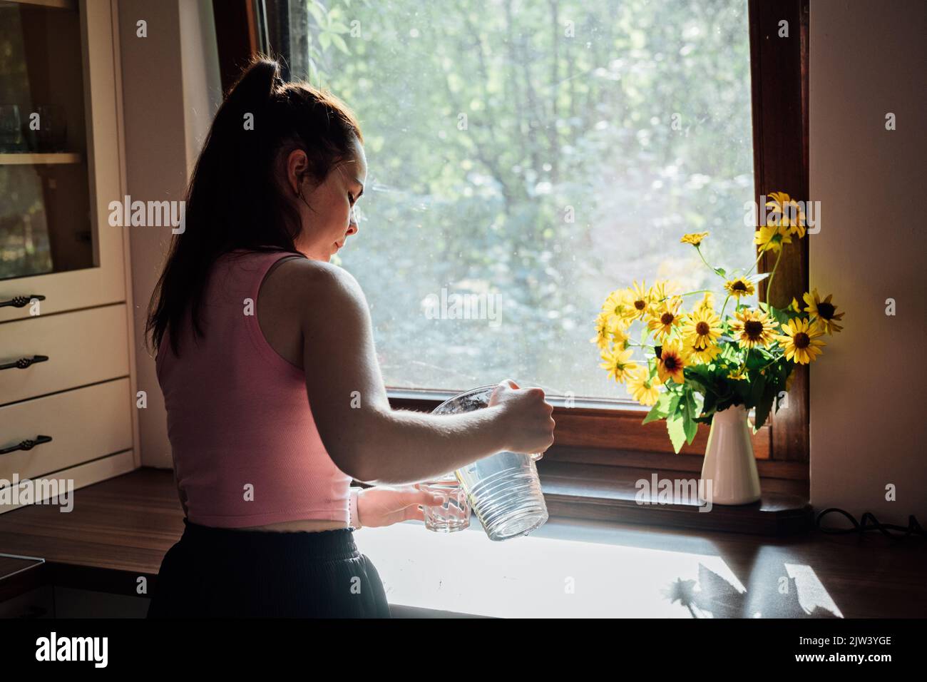Junge Frau trinkt Wasser aus Glas in der Küche. Kaukasisches weibliches Modell mit transparentem Glas in der Hand. Stockfoto
