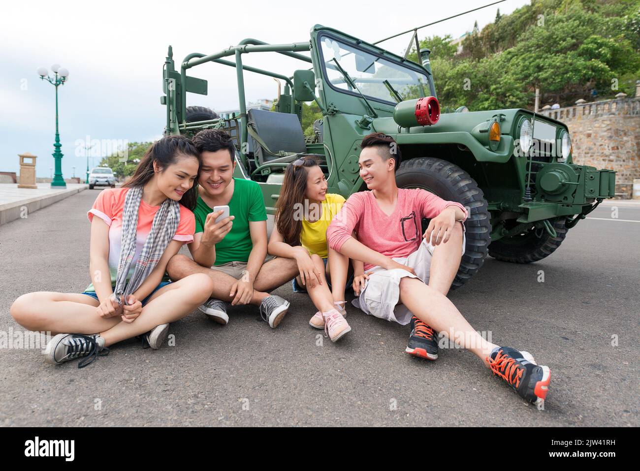 Gruppe asiatischer Touristen, die sich auf der Straße mit einem großen Jeep im Hintergrund ausruhen Stockfoto