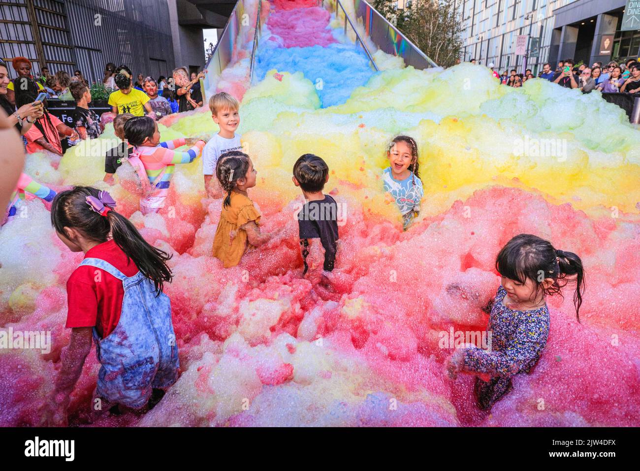 London, Großbritannien. 03. August 2022. Kinder haben Spaß im Schaum. Menschen interagieren mit 'Island of Foam: Version XVIII', einer farbenfrohen, sich ständig ändernden Schaumstoffanlage. Die Installation ist eine britische Premiere der deutschen Künstlerin Stephanie Lüning (die die „Schaumkanone“ oben auf der Treppe betreibt) und transformiert die Greenwich Peninsula mit Bergen aus regenbogenfarbenem Schaum. Kredit: Imageplotter/Alamy Live Nachrichten Stockfoto