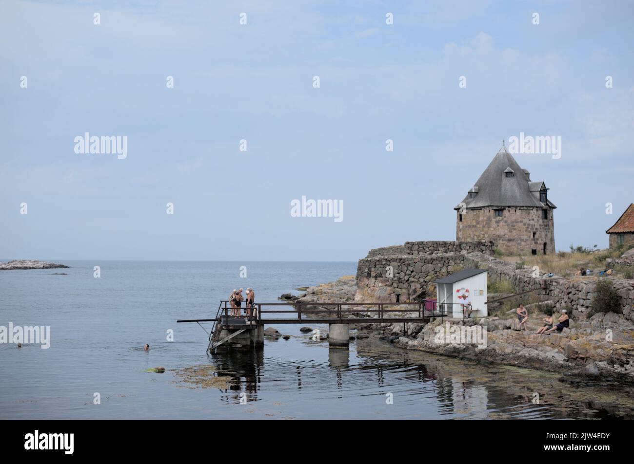 Badeplatz in Frederiksø (Christionsø) Dänemark. Ältere Menschen schwimmen. Felsiger Strand, Pier, alter Turm. Stockfoto