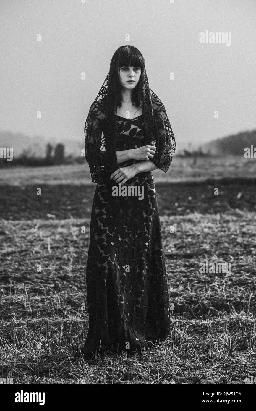Eine vertikale Graustufenaufnahme einer kaukasischen hübschen Frau in einem schwarzen Kleid im gotischen Stil Stockfoto