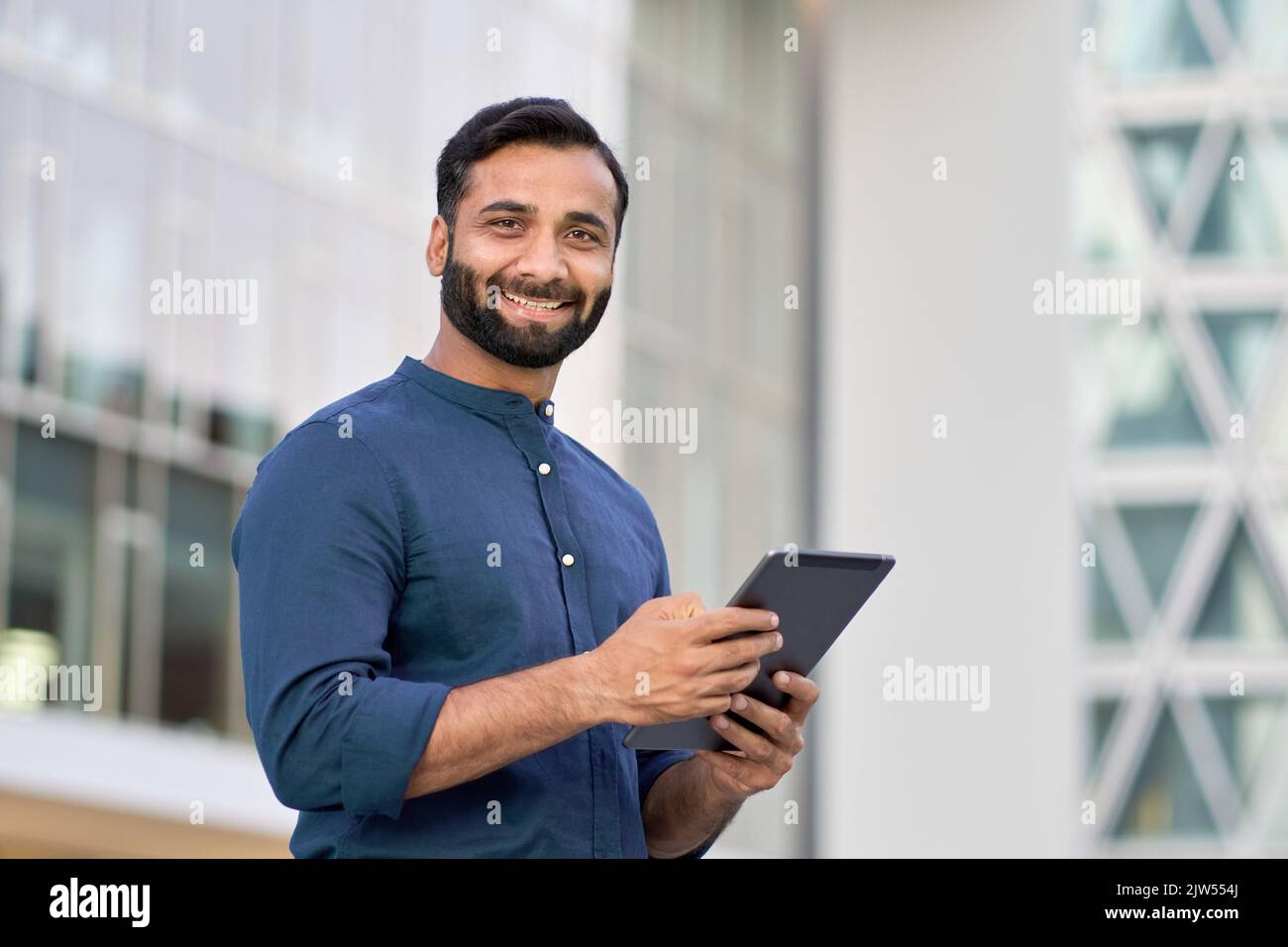 Lächelnder indischer Geschäftsmann, der im Freien ein digitales Tablet verwendet. Stockfoto