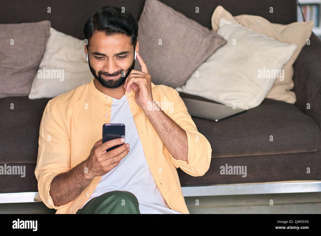 Indischer Mann sitzt zu Hause auf dem Sofa mit dem Handy und schaut sich Videos an. Stockfoto