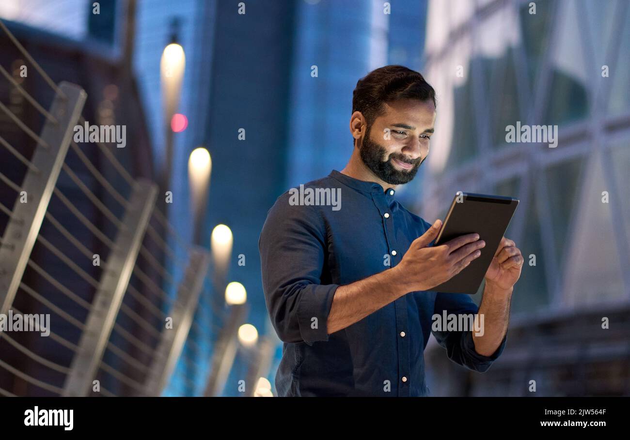 Reicher erfolgreicher indischer Geschäftsmann, der in der Nachtstadt mit einem digitalen Tablet steht. Stockfoto