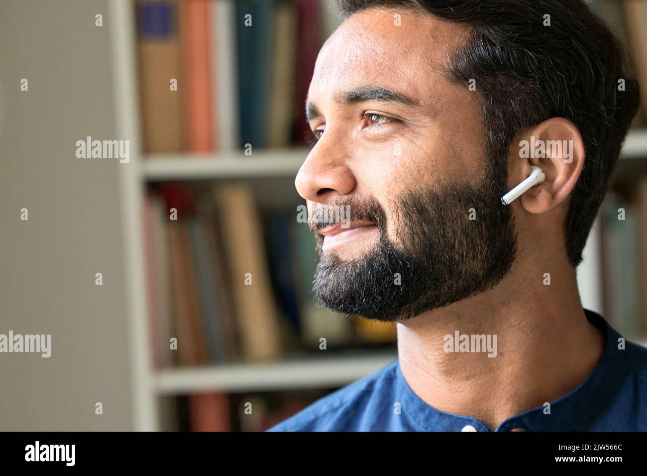 Lächelnder indischer Mann mit Ohrstöpsel, der Musik oder Podcast hört. Nahaufnahme Stockfoto