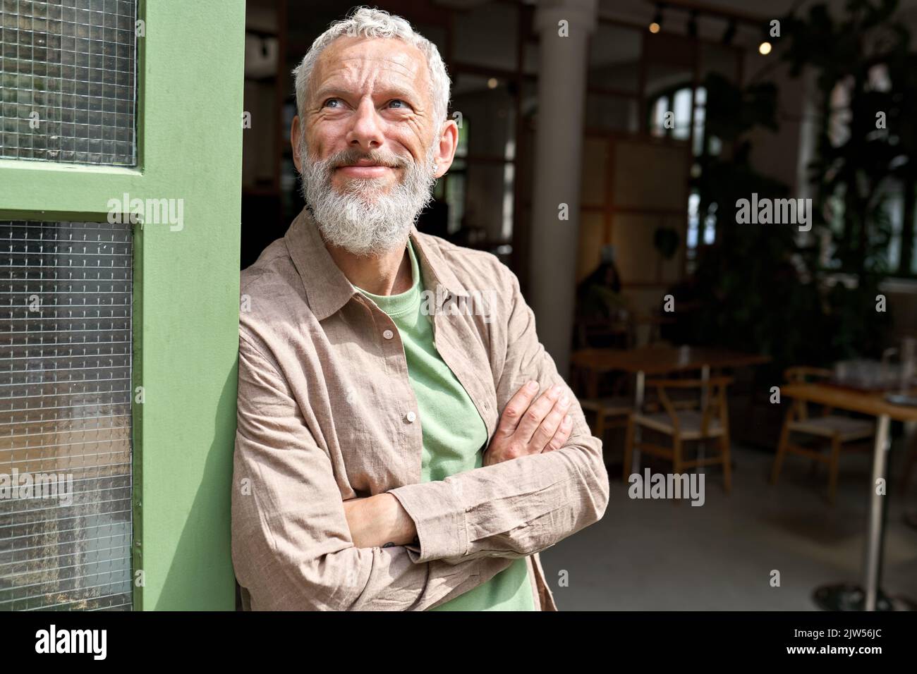 Glücklicher, selbstbewusster europäischer, älterer Mann, Inhaber von Kleinunternehmen, der vor dem Café steht. Stockfoto