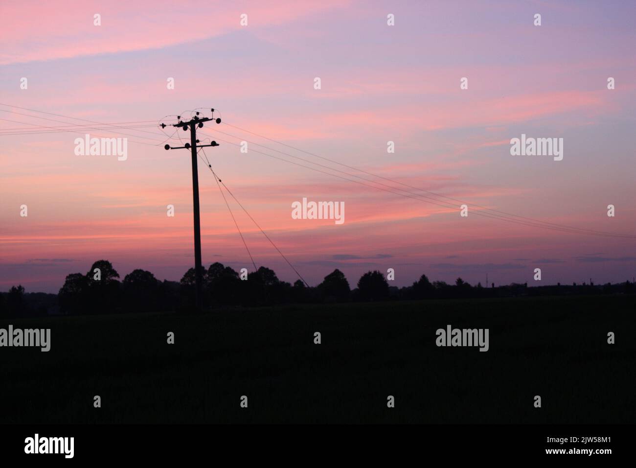 Sonnenuntergang mit der Silhouette eines Telegrafenmastes und Kabeln in der Landschaft von Essex Stockfoto