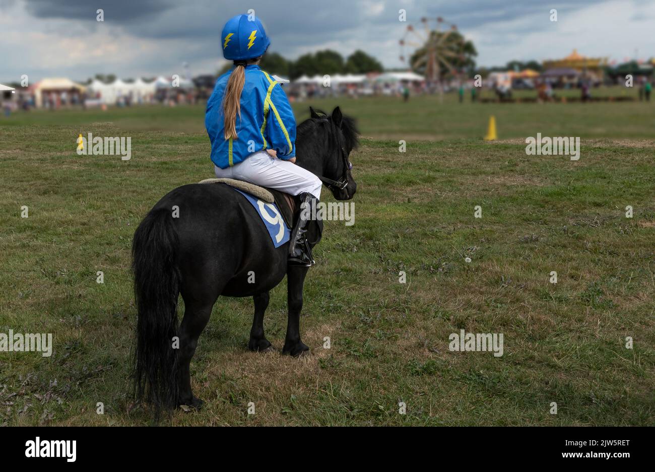 Junge Person in blau und gelb gekleidet als Jockey auf einem schwarzen Pony Stockfoto