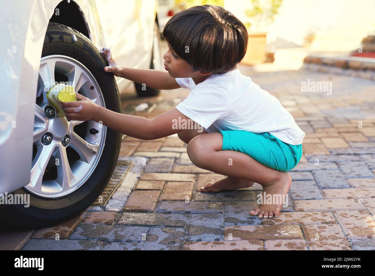 Dieses Auto wird wieder wie neu aussehen. Ein kleiner Junge wäscht ein Rad von einem Auto. Stockfoto