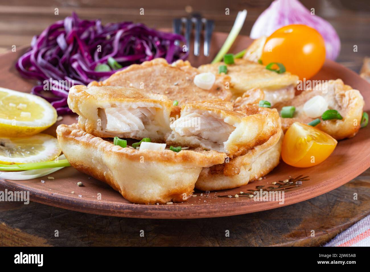 Saftige, schmackhafte, gesunde Lebensmittel. Vorder- und Nahansicht mehrerer Fischstücke, die mit gelben Kirschtomaten, Zitrone, Knoblauch, Lauch und rotem cabb geschlagen werden Stockfoto