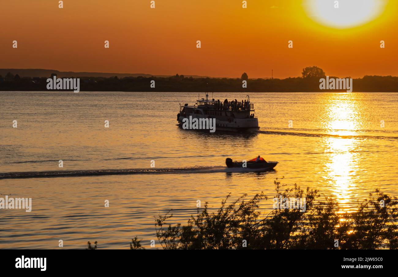 Sonnenuntergang Flussschiff und Motorboot Silhouette Ansicht. Selektiver Fokus. Natürlicher Hintergrund, orange Farben am Himmel und auf dem Wasser von heller Sonne. Stockfoto