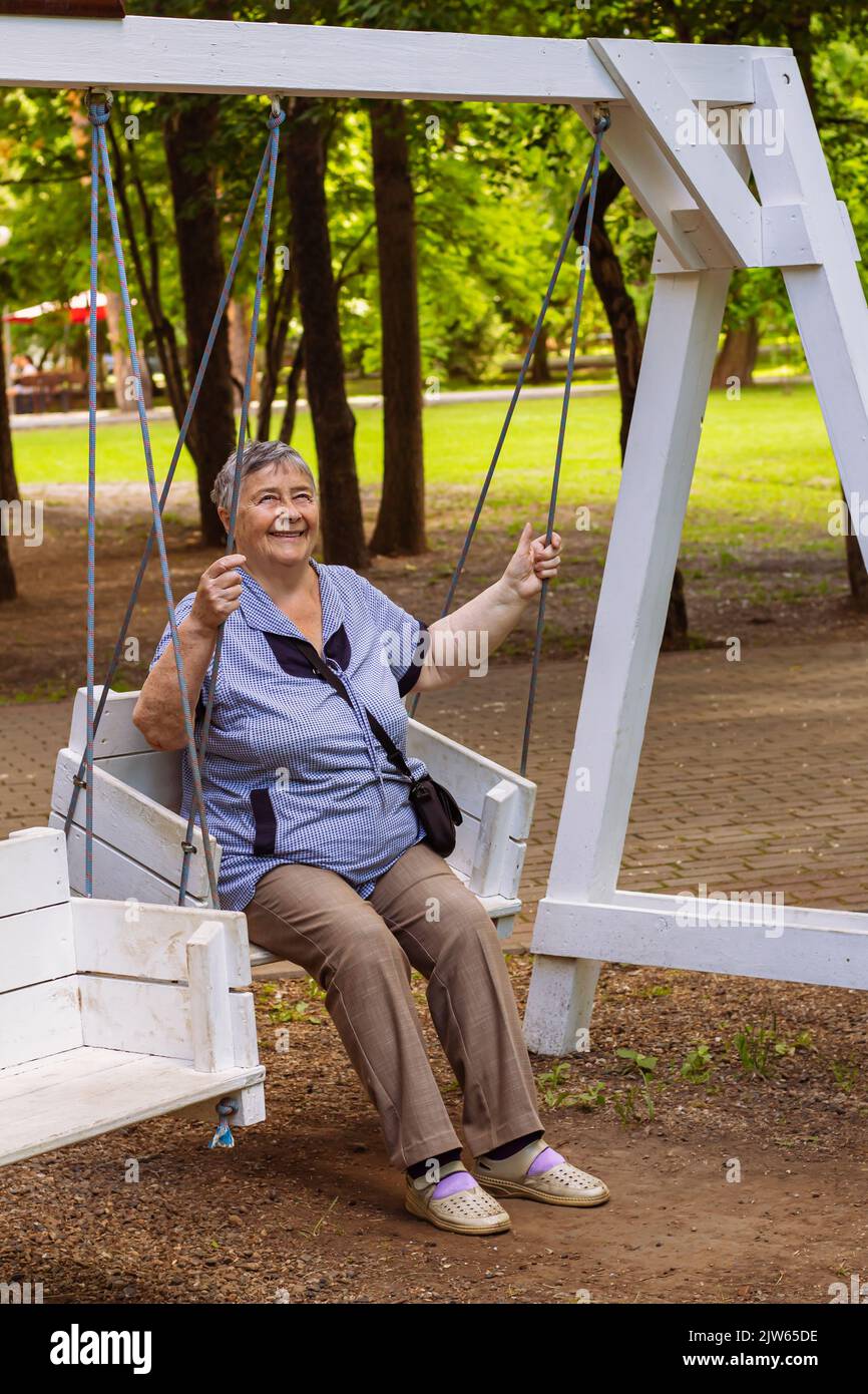 Verspielte und glückliche Frau genießen bei Schaukel im Freien in Park oder Garten entspannt lachen, alte Menschen freudig aktiven Ruhestand und Entspannungskonzept. Stockfoto
