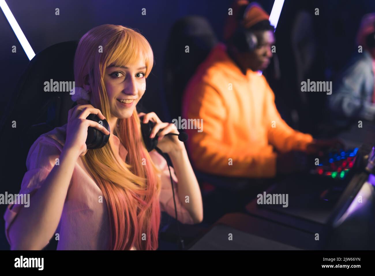 Junge asiatische Frau mit niedlichen gefärbten Zöpfen halten Headset um den Hals spielen Online-Spiel mit Freunden Blick in die Kamera lächelnd. Horiontital-Schuss. Hochwertige Fotos Stockfoto