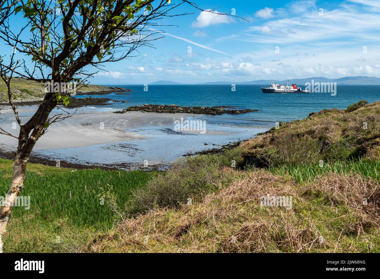 Die kaledonische MacBrayne Fähre 'Hebridean Isles' nähert sich der Insel Colonsay auf dem Weg von Islay, mit sandigen Queen's Bay Strand im Vordergrund. Stockfoto