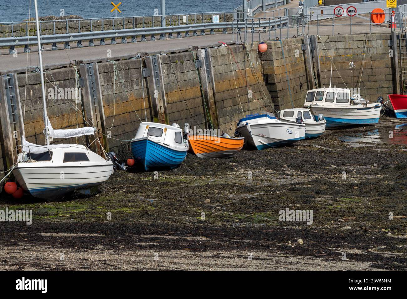 Reihe von kleinen Booten bei Ebbe, die neben dem Pier im Scalasaig Harbour auf der abgelegenen Hebriden-Insel Colonsay, Schottland, Großbritannien, vertäut sind Stockfoto