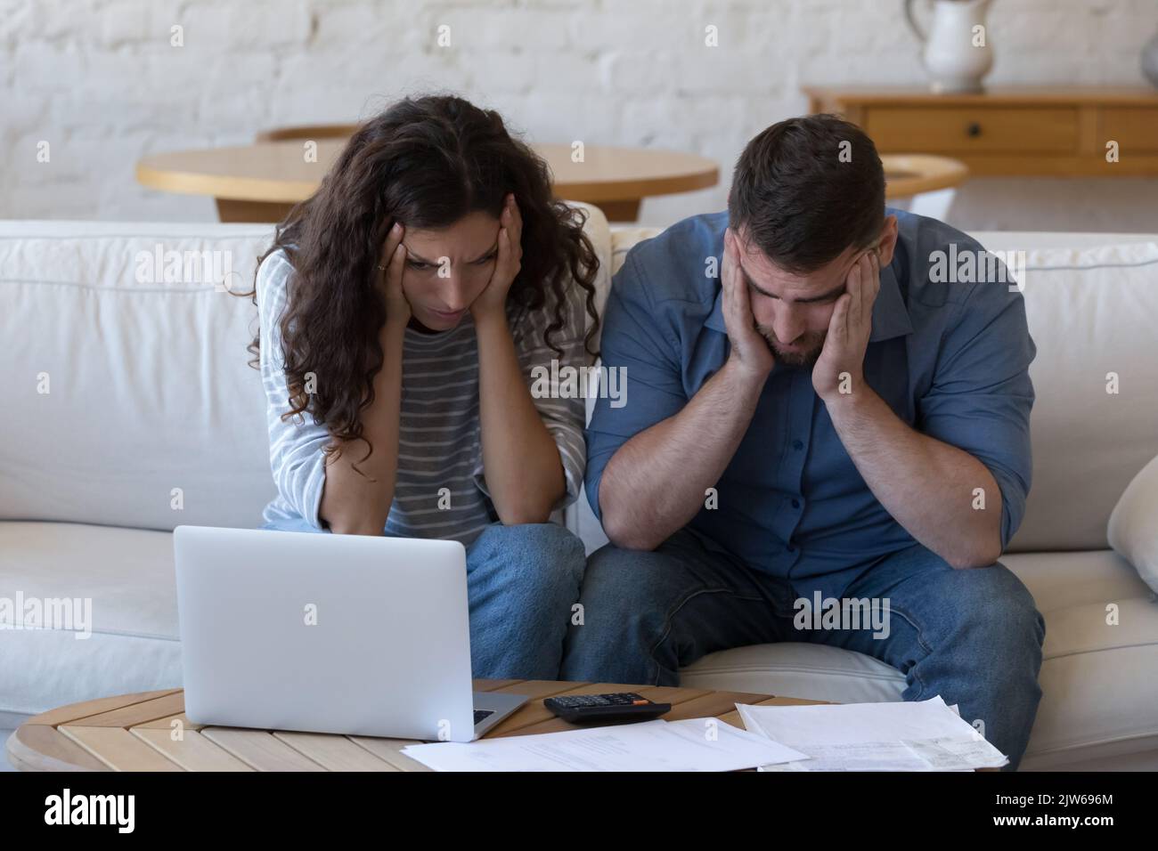 Verzweifeltes Paar sitzt am Tisch mit Haufen unbezahlter Rechnungen Stockfoto