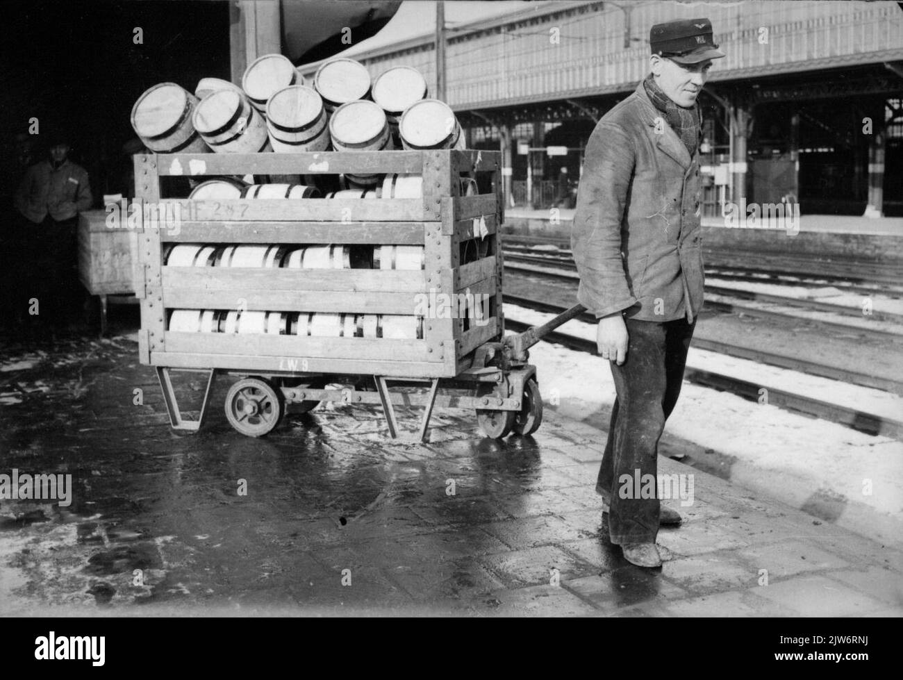 Bild eines Mitarbeiters von Van Gend & Loos mit einem Wagen mit Fässern auf der Plattform für Expressgüter der N.S. Station Utrecht et al. In Utrecht. Stockfoto