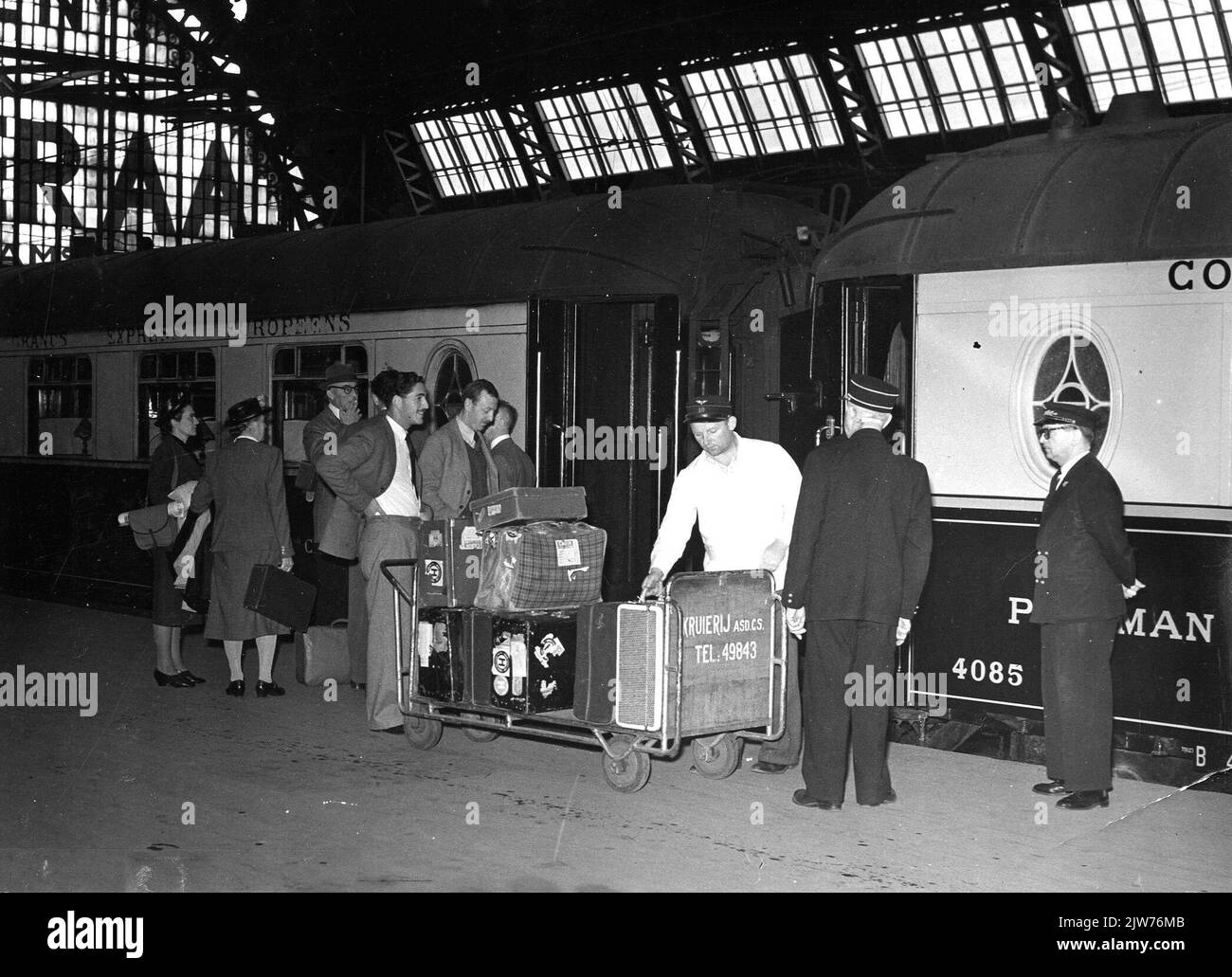 Abbildung eines Portiers mit einem Gepäckwagen eines Zuges aus Wagen der Internationalen des Wagons-Lits (Restaurierungswagen Nr. 4085) auf einer Plattform des N.S. Bahnhofs Amsterdam et al. In Amsterdam. Stockfoto