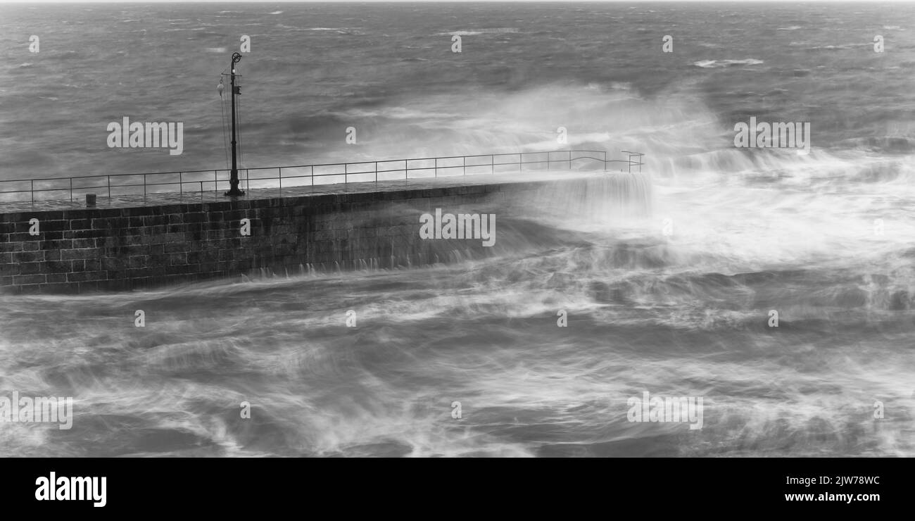 Große Wellen schlagen in und über dem Porthleven Pier. Stockfoto