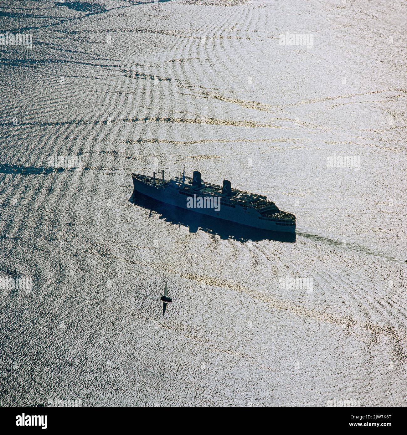 New York, 1980s, Britanis Schiff Liner Silhouette, winziges Segelboot, Licht Reflexionen Wasser, obere New York Bay, Luft, New York City, NYC, NY, USA, Stockfoto