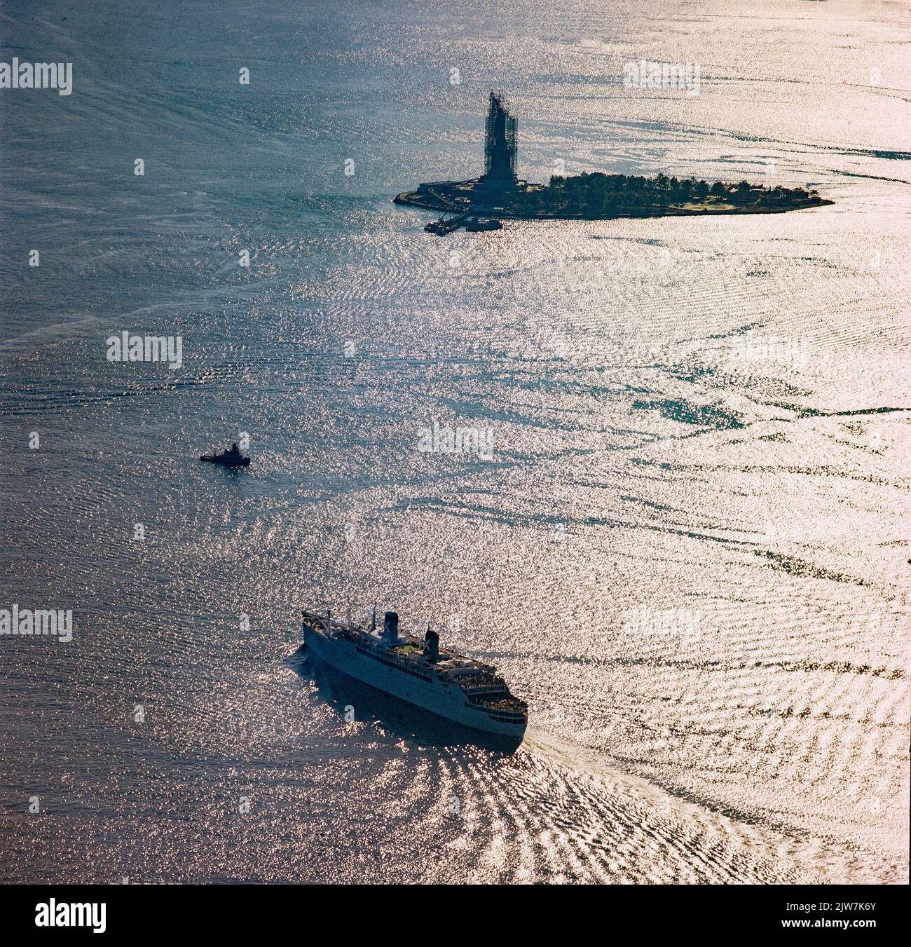 New York, 1980er, Britanis-Schiff, Liberty Island in der Ferne, Freiheitsstatue mit Renovierungsgerüsten, Lichtreflexionen auf dem Wasser, obere New Yorker Bucht, Luft, New York City, NYC, NY, USA, Stockfoto