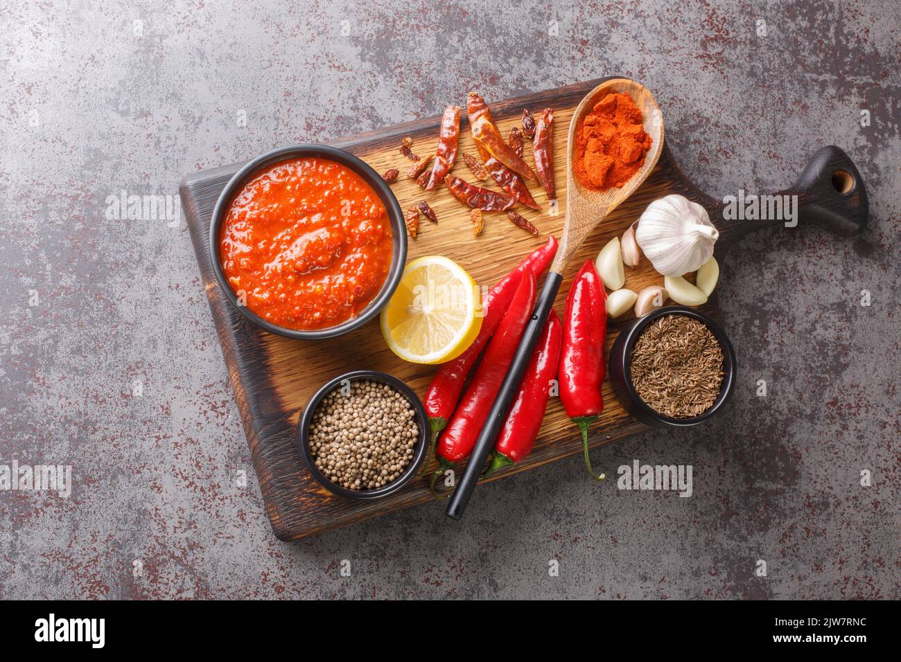 Scharfe Chili-Pfeffer-Sauce Paste Harissa, arabische Küche Adjika auf der Schüssel auf Holzbrett mit Zutaten Nahaufnahme. Horizontale Draufsicht von oben Stockfoto