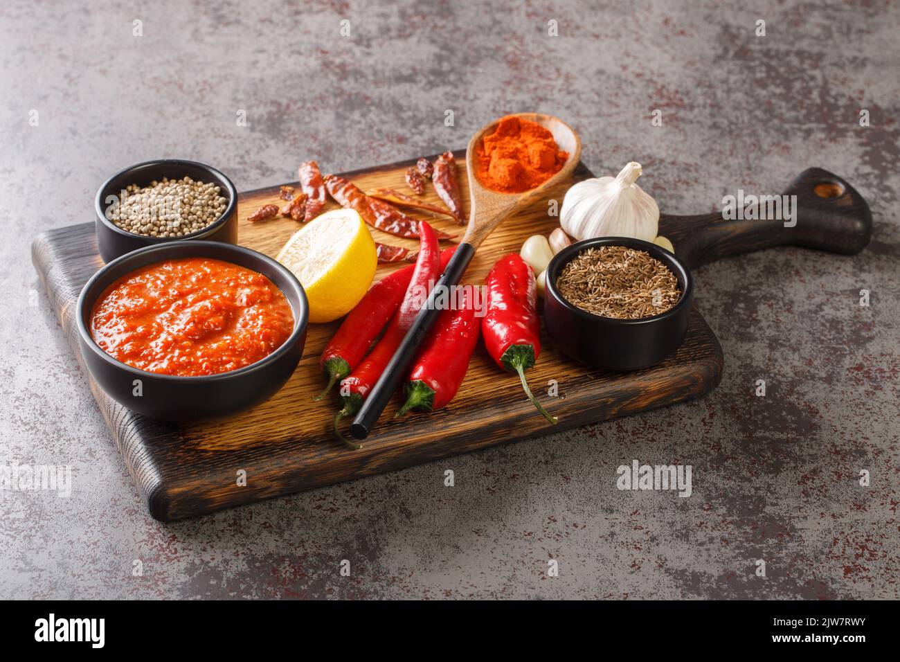 Scharfe Chili-Pfeffer-Sauce Paste Harissa, arabische Küche Adjika auf der Schüssel auf Holzbrett mit Zutaten Nahaufnahme. Horizontal Stockfoto