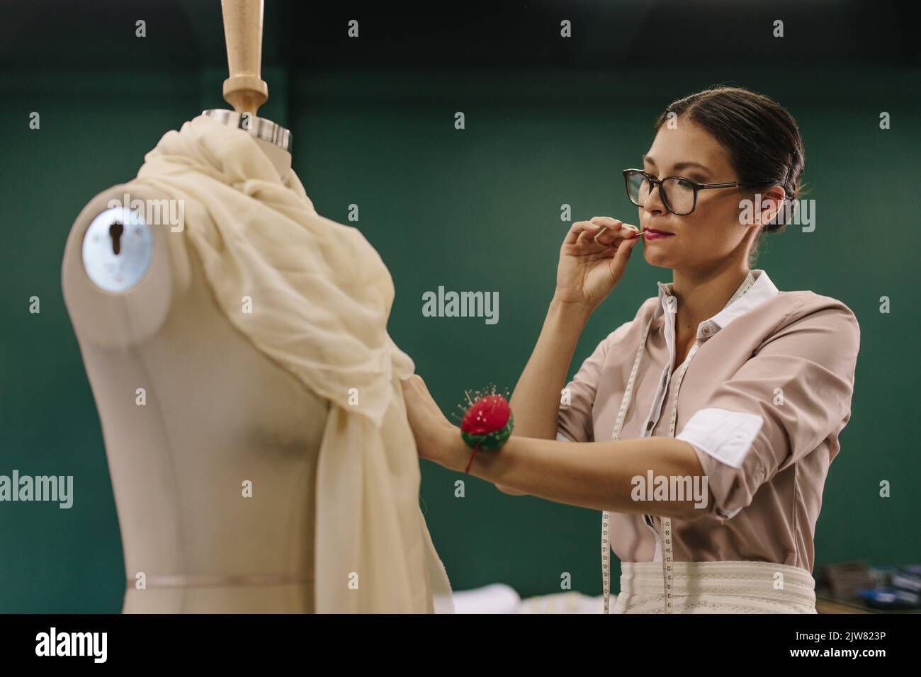 Asiatische weibliche Designerin, die an Schaufensterpuppe arbeitet. Schneiderin legt Nadeln im Studio auf ein Kleid. Stockfoto