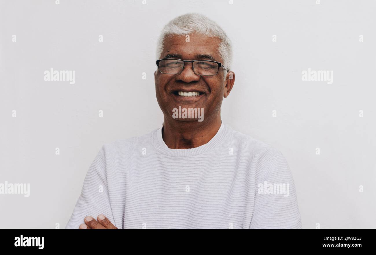 Glücklicher älterer Mann, der vor einem weißen Hintergrund vor der Kamera lächelt. Porträt eines fröhlichen, reifen Mannes mit Brille. Stockfoto