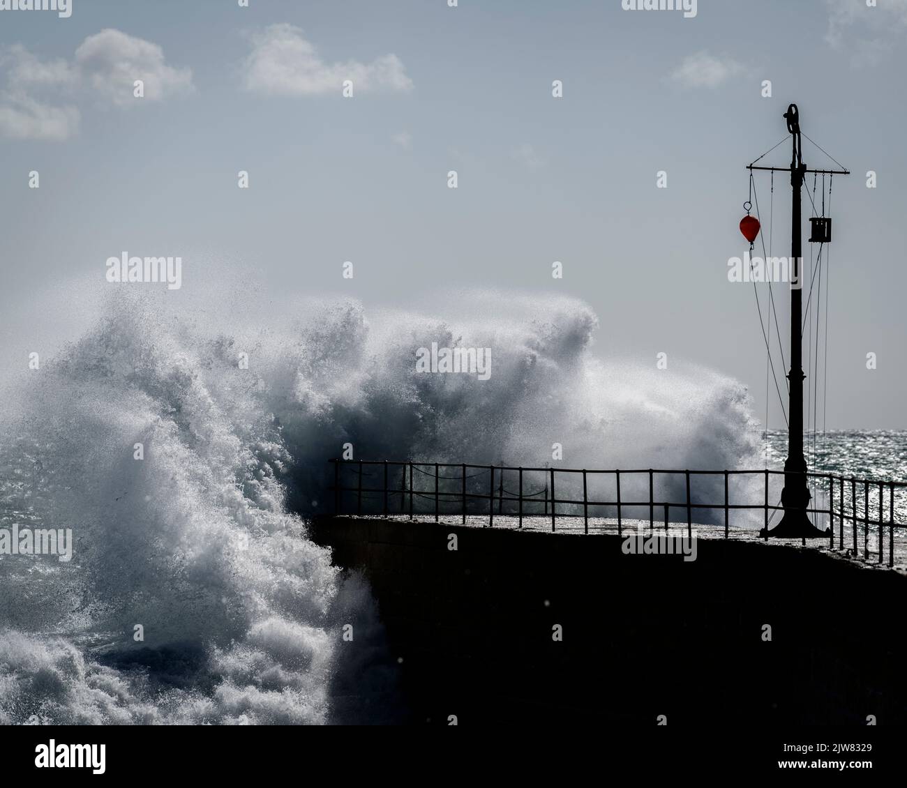 Als ein Sturm die Küste von Cornwall trifft, nimmt der Pier am Hafen von Porthleven die Kraft der Wellen auf, während sie hart treffen. Stockfoto