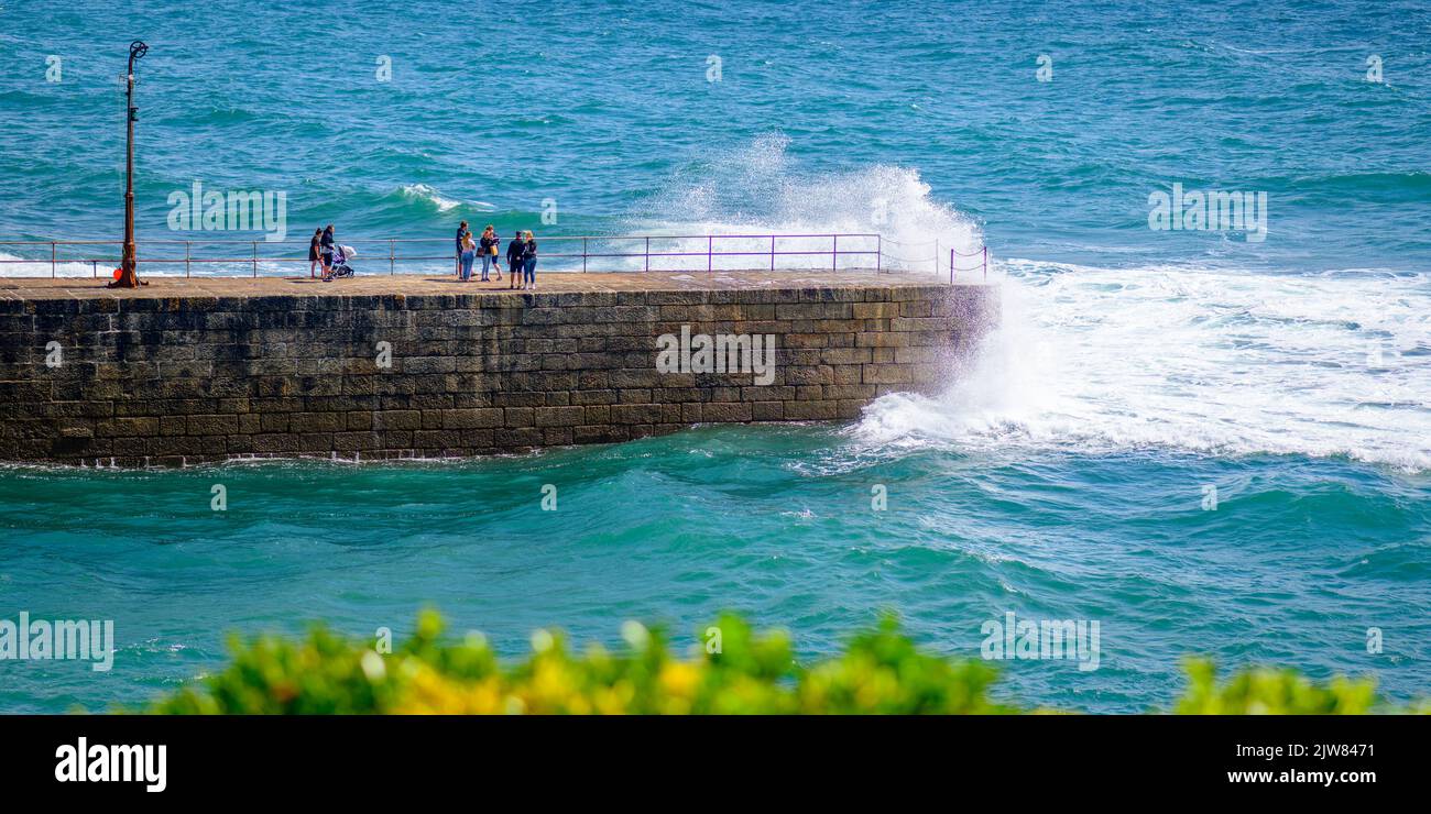 Touristen werden von großen Wellen, die über dem Porthleven Pier krachen, erwischt. Stockfoto
