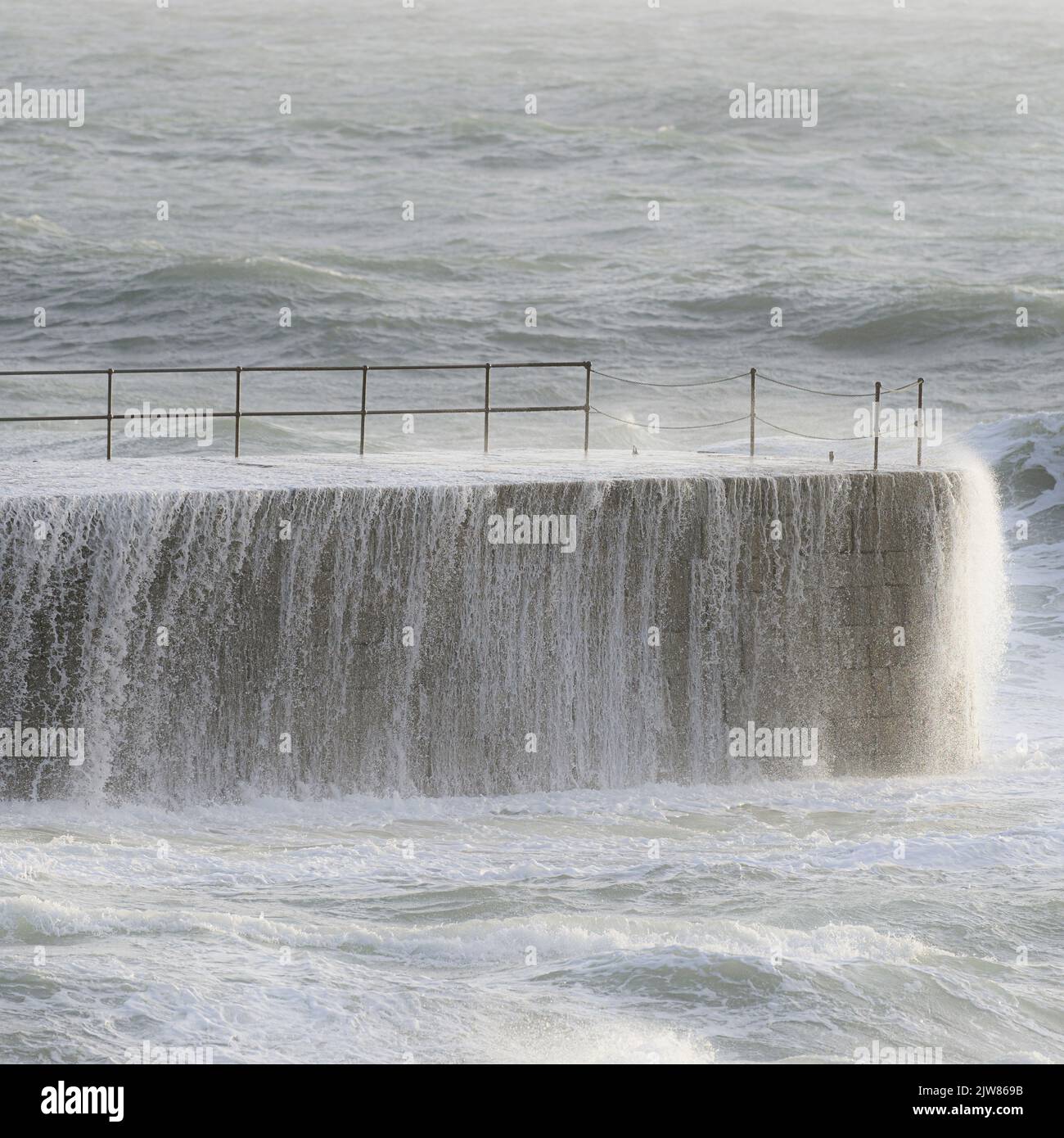 Als ein Sturm die Küste von Cornwall trifft, nimmt der Pier am Hafen von Porthleven die Kraft der Wellen auf, während sie hart treffen. Stockfoto