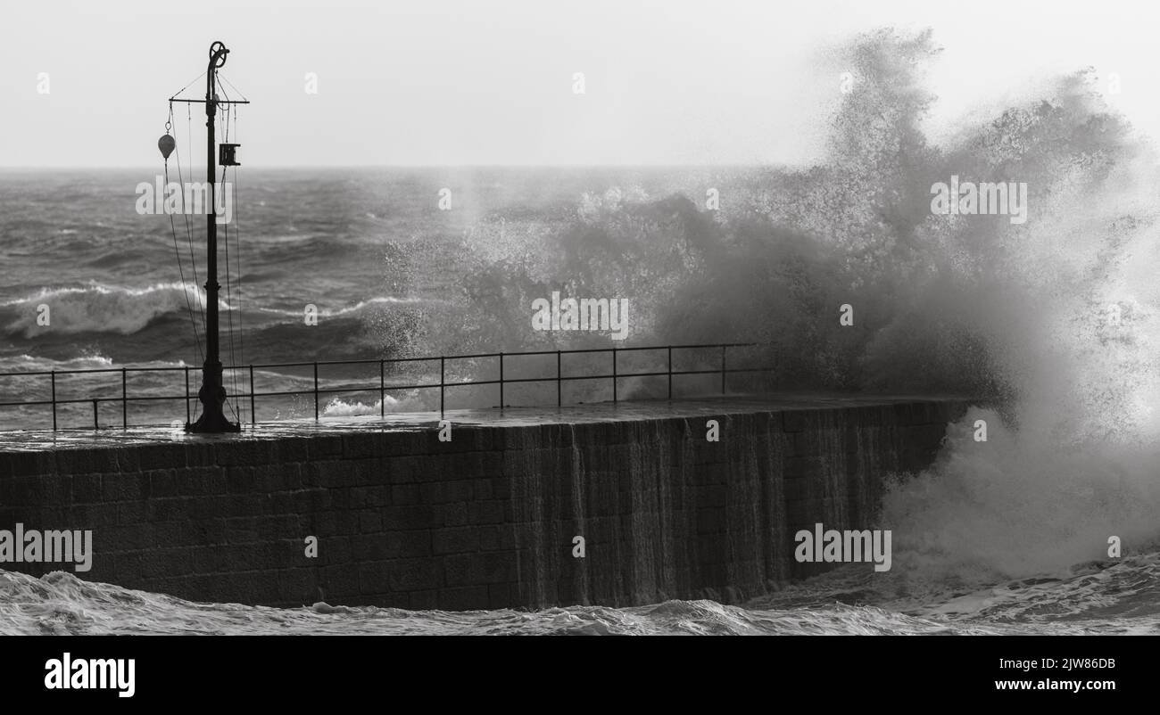 Große Wellen schlagen in und über dem Porthleven Pier. Stockfoto