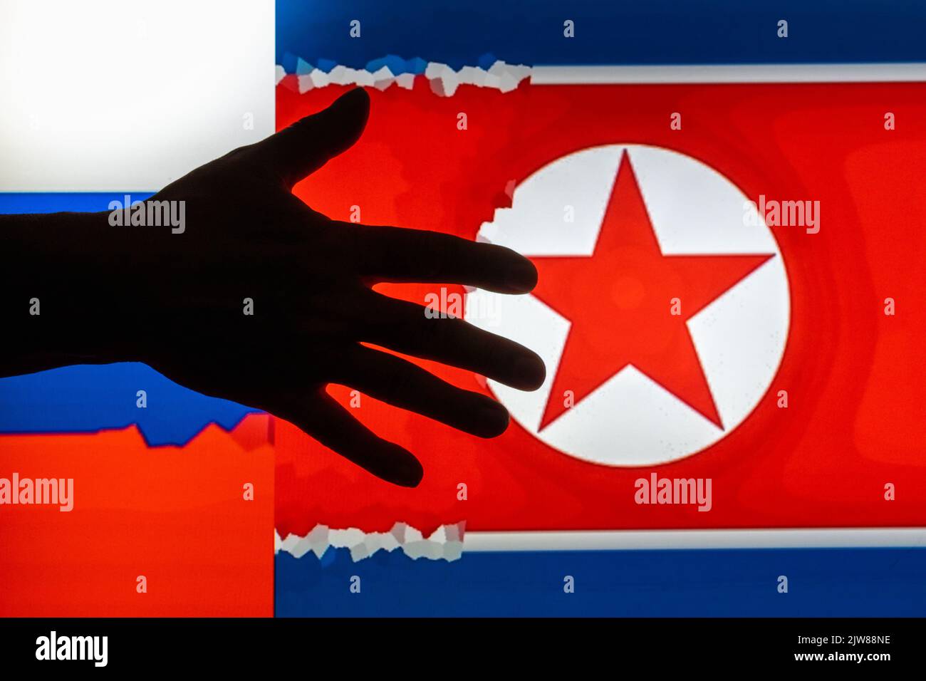 Dunkle Silhouette ausgestreckter Hand auf unscharfem digitalen Bildhintergrund von Flaggen der Russischen Föderation und Nordkoreas Stockfoto