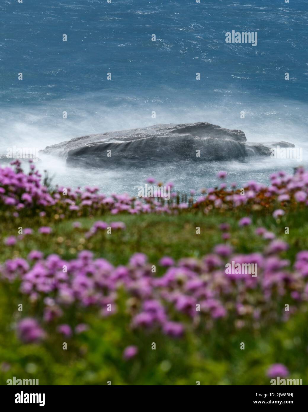 Eine Zeitlupenaufnahme der Wellen, die über die Felsen am Fuße der Porthleven-Klippe krachen. Stockfoto