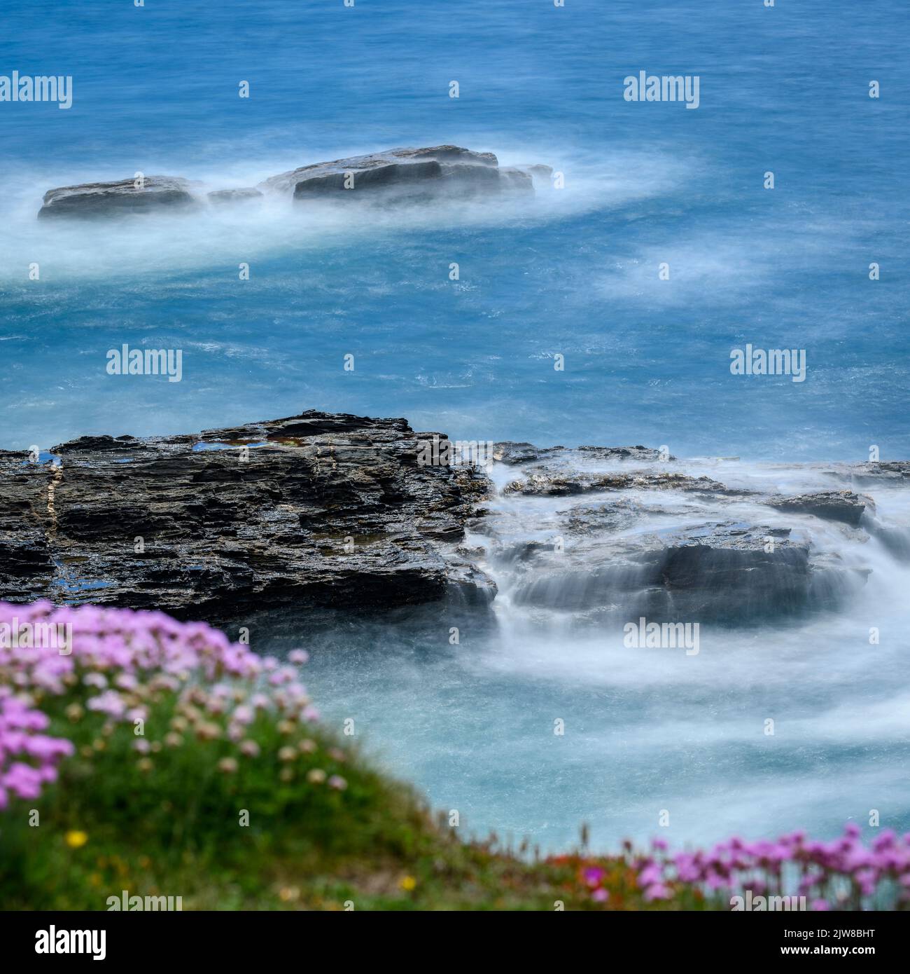 Eine Zeitlupenaufnahme der Wellen, die über die Felsen am Fuße der Porthleven-Klippe krachen. Stockfoto