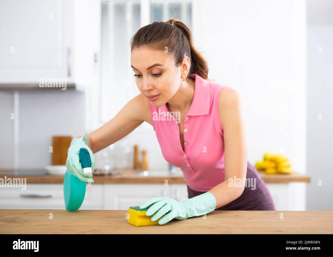 Junge Frau mit Handschuhen wäscht die Arbeitsplatte in der Küche Stockfoto