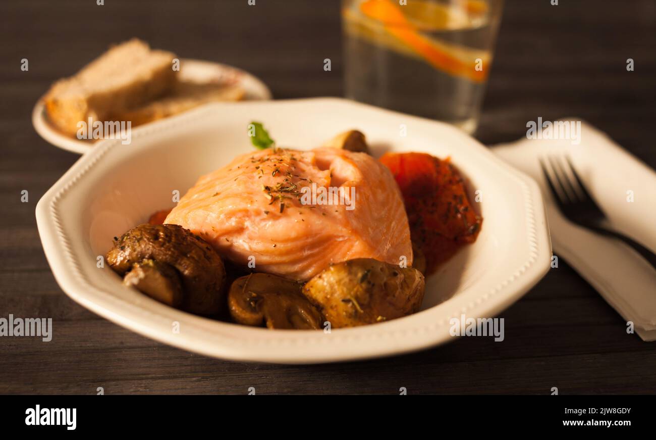 Gedünstetes Lachsfilet auf einem Kissen aus gebratenen Pilzen und Tomaten in einer weißen Schüssel Stockfoto