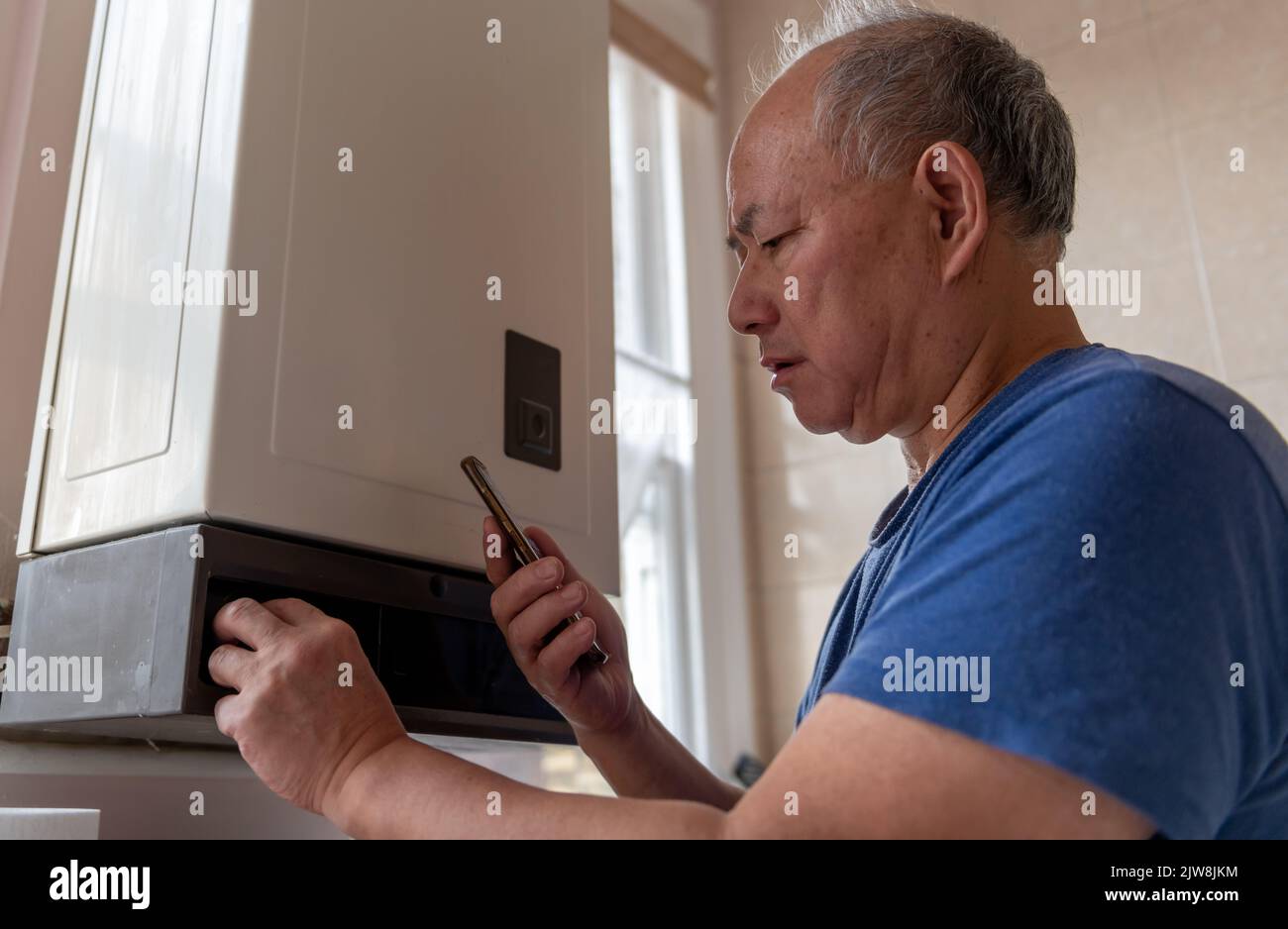 Ein leitender Mann, der den Warmwasserboiler herunterdrehte, um Geld zu sparen und versuchte, mit dem dramatischen Anstieg der Energiekosten fertig zu werden. Stockfoto