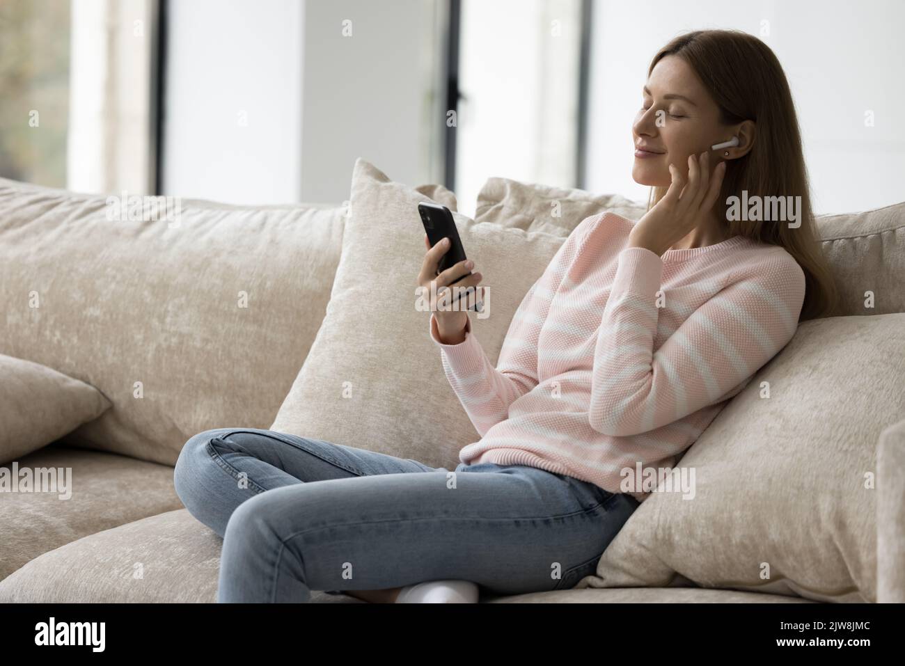 Friedlicher Handy-Nutzer, der sich auf der Couch mit geschlossenen Augen entspannt Stockfoto