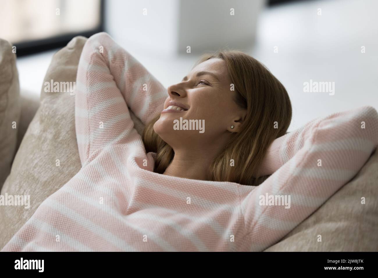 Glückliche kaukasische Frau, die sich zu Hause auf dem gemütlichen Sofa entspannt Stockfoto