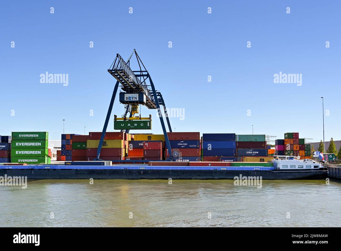 Rotterdam, Niederlande - August 2022: Großer mobiler Kran, der einen Container von einem Industriekahn auf dem Fluss in der Nähe von Rotterdam hebt Stockfoto